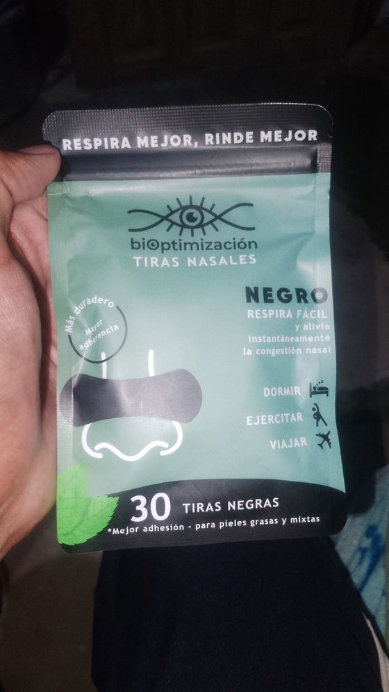 Mano sosteniendo el pack de tiras nasales negras sobre fondo oscuro