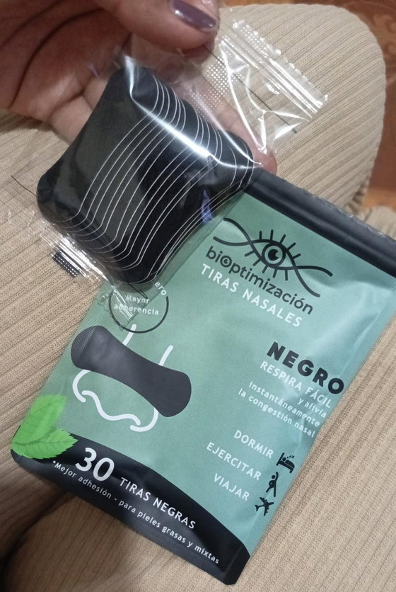 Tiras nasales negras sueltas junto a su pack, sobre una cama